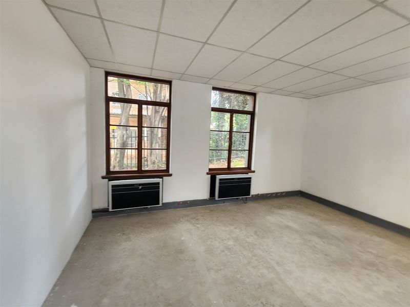 An empty office space featuring a suspended ceiling, timber-framed windows, and integrated under-window HVAC units, ready for flooring installation and fit-out.
