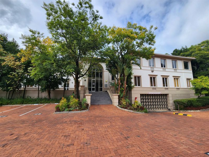 Front exterior view of a professional office building featuring a brick paved driveway, landscaped gardens, and a prominent arched glass entrance.