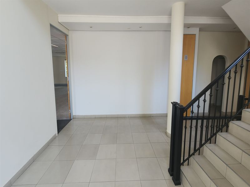 A bright and spacious office entrance area featuring tiled flooring, a central structural column, and a staircase with a decorative wrought iron balustrade.