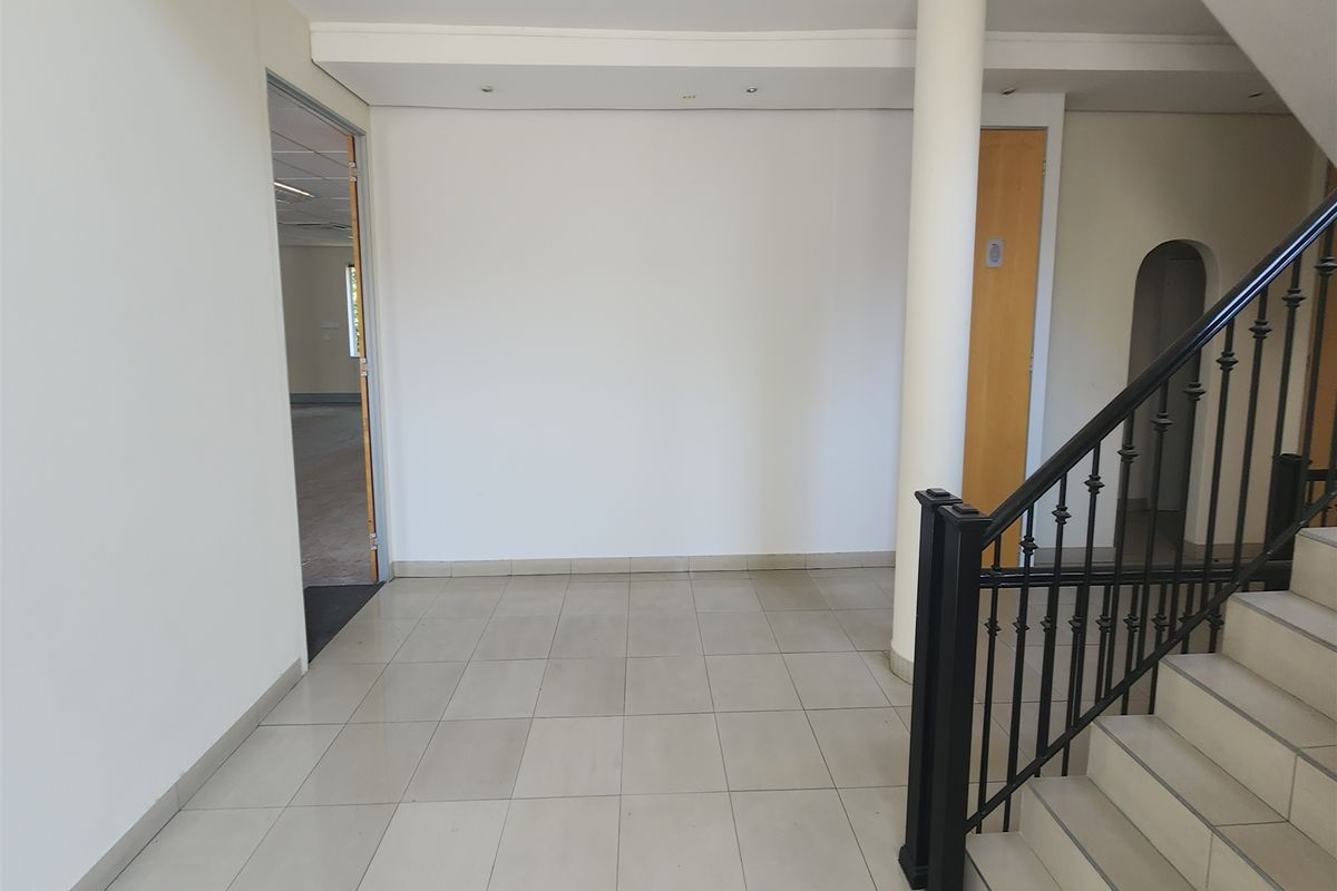 A bright and spacious office entrance area featuring tiled flooring, a central structural column, and a staircase with a decorative wrought iron balustrade.