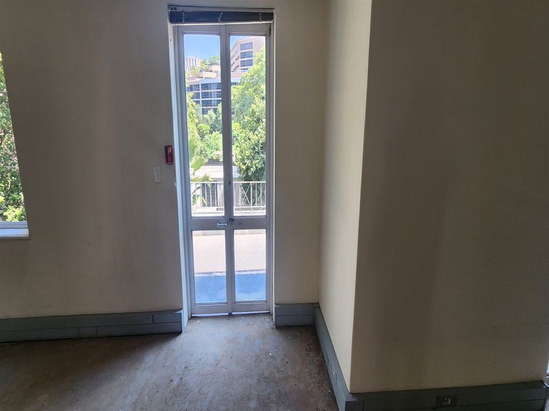 An empty office space featuring a glass door leading to a balcony, with neutral walls and worn flooring.