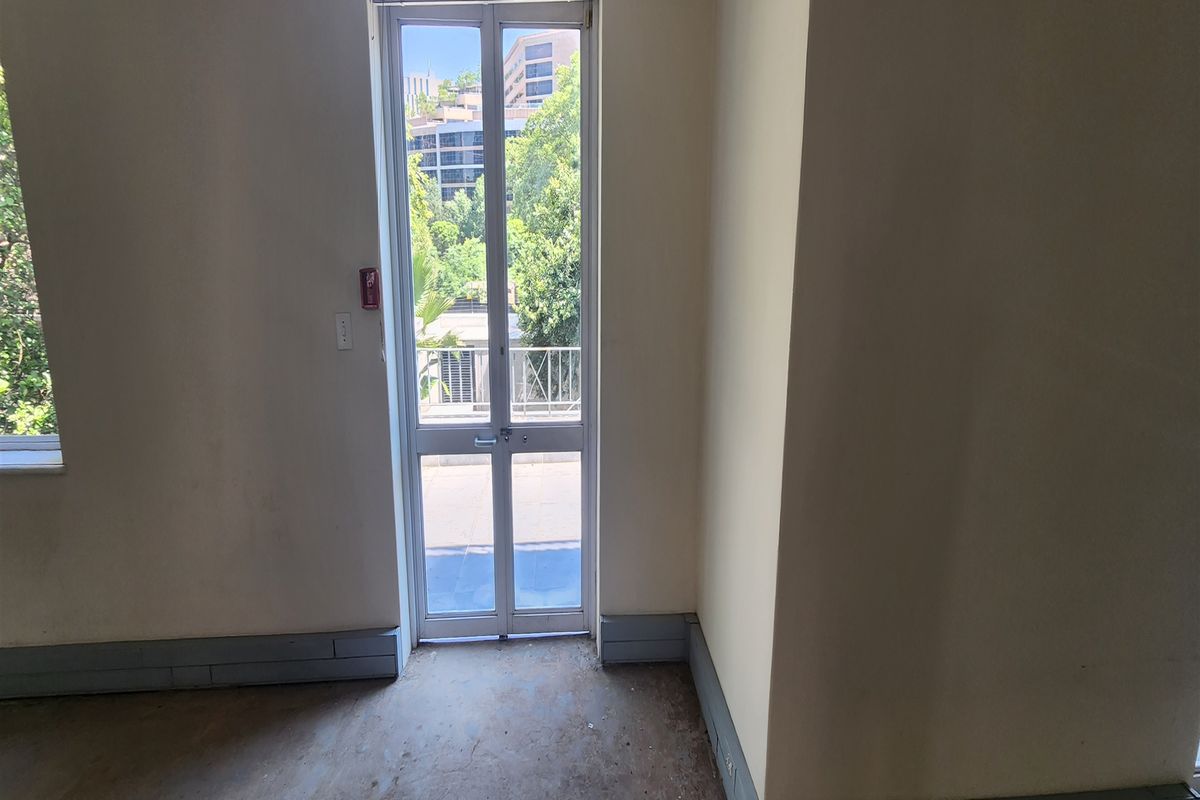 An empty office space featuring a glass door leading to a balcony, with neutral walls and worn flooring.