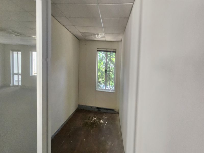 A vacant office space featuring a suspended ceiling, window, and baseboard heating, currently requiring floor and wall maintenance.