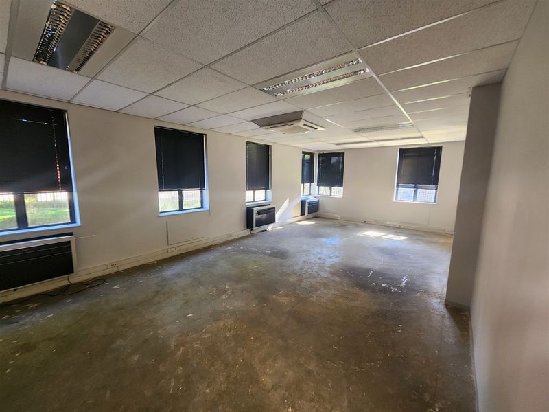 An empty office space featuring suspended ceilings, recessed lighting, wall-mounted air conditioning units, and exposed concrete flooring.