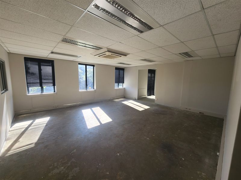 An empty, open-plan office space featuring a suspended ceiling with recessed lighting, ducted air conditioning, and large windows with fitted venetian blinds.
