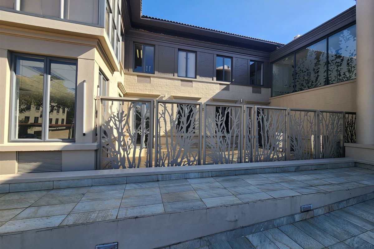 A well-maintained rear courtyard area featuring stone paving, decorative laser-cut metal privacy screens, and modern aluminium-framed windows.