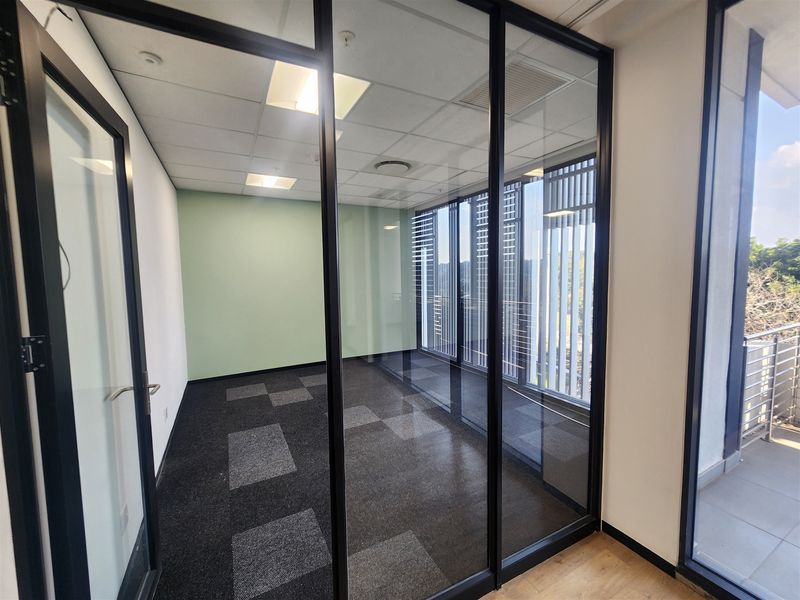 A modern, empty office space featuring glass partition walls, carpet tiles, and a suspended ceiling with recessed lighting.