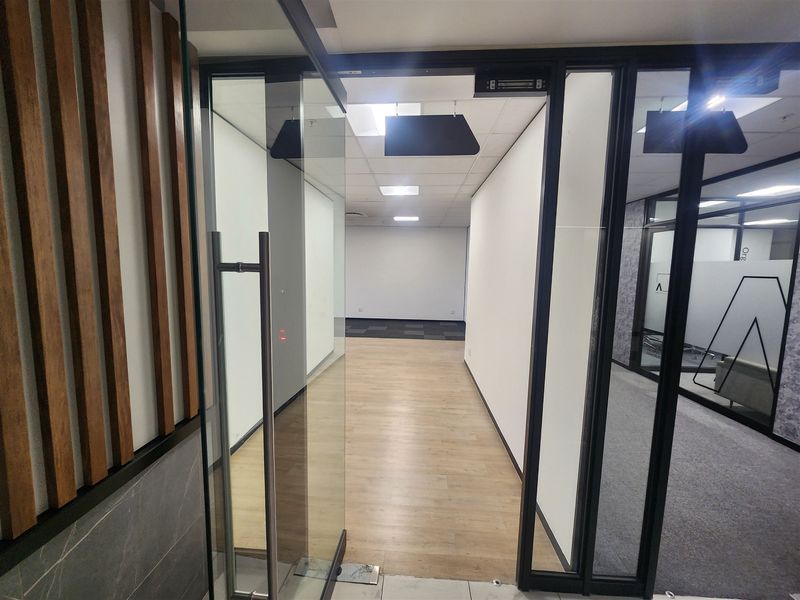Modern office entrance featuring a glass door, timber slat wall detailing, and clean, neutral finishes throughout the vacant workspace.