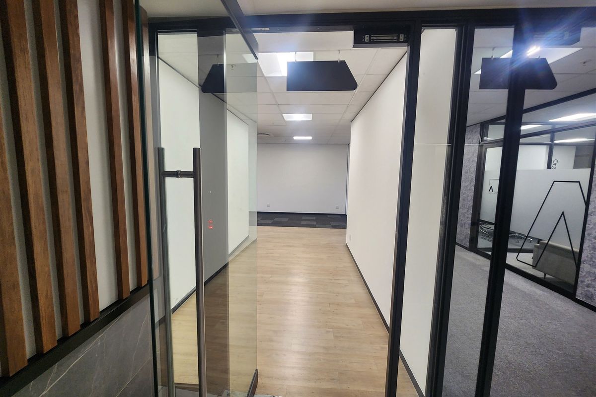 Modern office entrance featuring a glass door, timber slat wall detailing, and clean, neutral finishes throughout the vacant workspace.