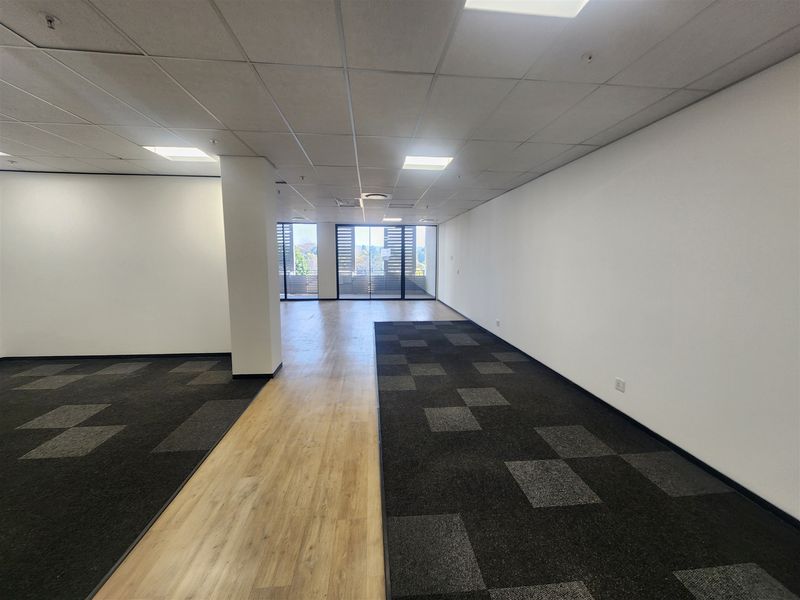 Spacious, open-plan office area featuring a mix of carpet and laminate flooring, recessed ceiling lights, and large sliding glass doors providing natural light.
