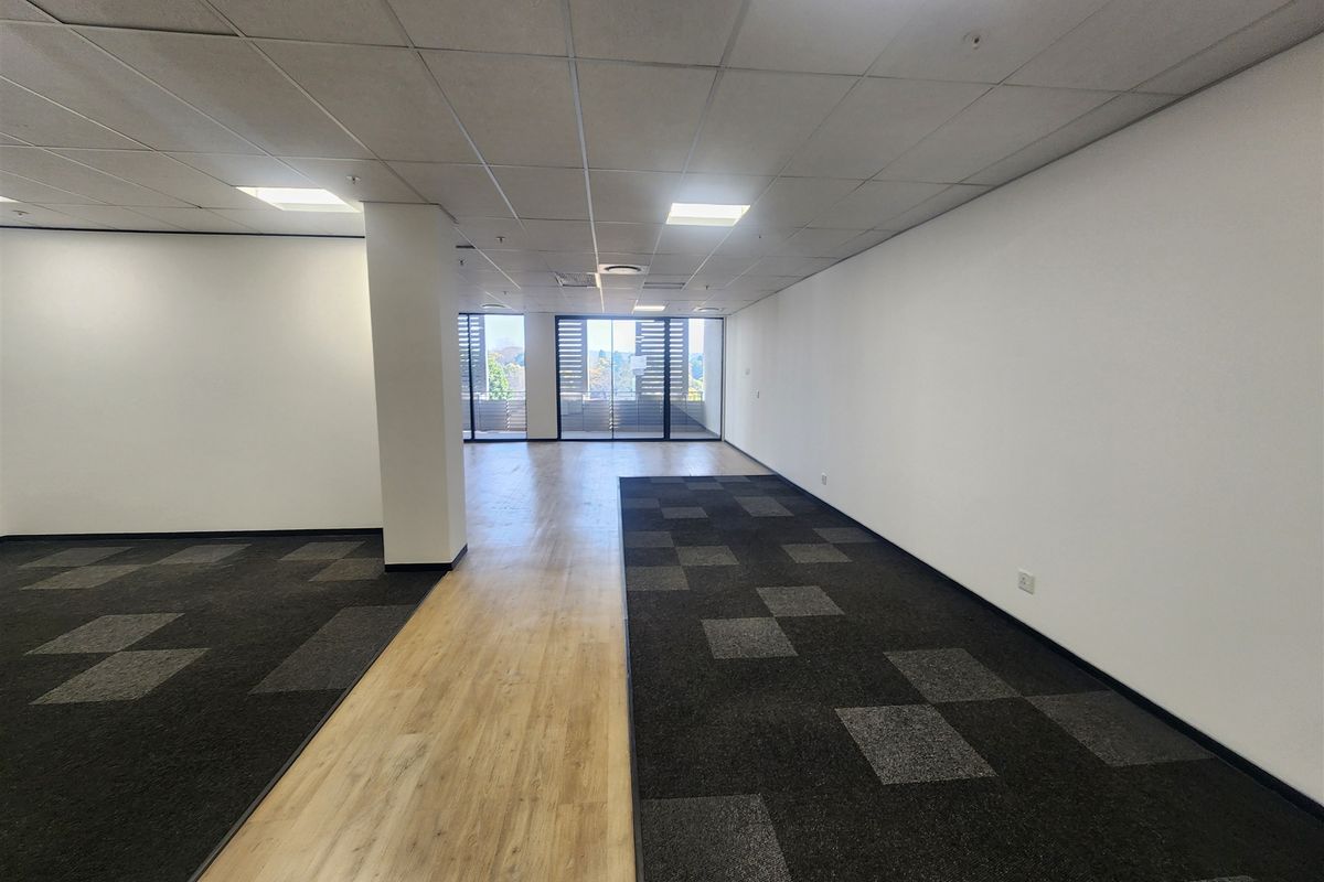 Spacious, open-plan office area featuring a mix of carpet and laminate flooring, recessed ceiling lights, and large sliding glass doors providing natural light.