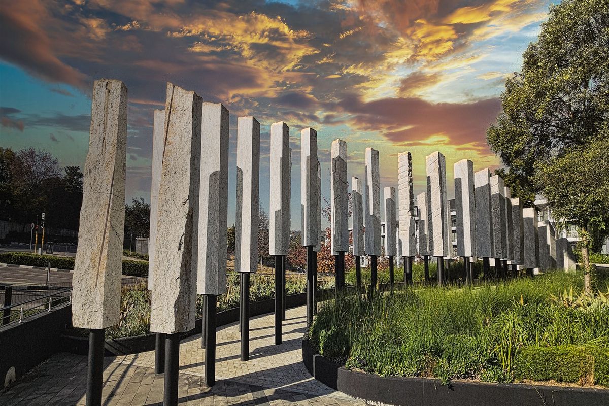 A modern landscaped exterior area featuring a row of stone pillar sculptures, paved pathways, and manicured garden beds at the office property entrance.