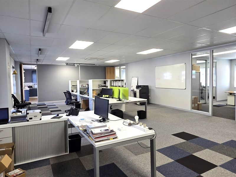 A spacious, well-lit open-plan office area featuring modern carpet tiles, suspended ceilings, and glass partitioning for a professional workspace environment.