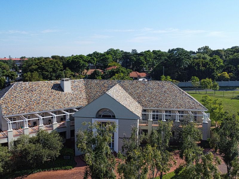 Aerial view of a professional office building featuring a multi-pitched tiled roof, covered patio areas, and extensive landscaped grounds.