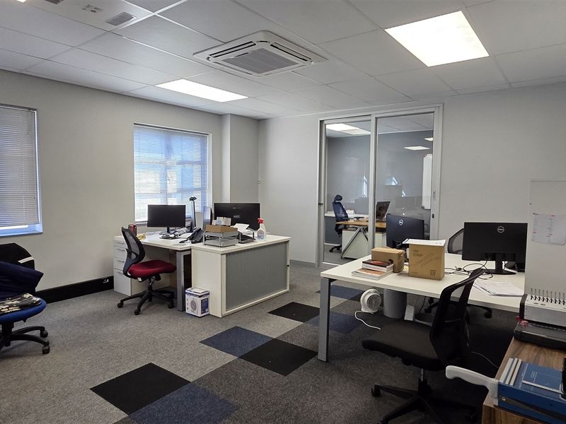A functional office space featuring carpet tiles, a suspended ceiling with recessed lighting, ducted air conditioning, and a sliding glass partition.