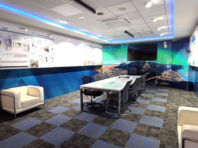Modern office boardroom featuring a suspended ceiling with integrated LED lighting, cassette air conditioning, and professional wall-mounted product display panels.