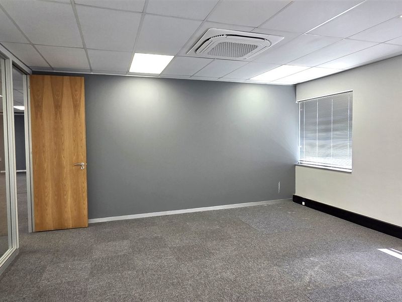 A clean, professional office space featuring carpet tiles, a suspended ceiling with integrated air conditioning, and large windows with venetian blinds.