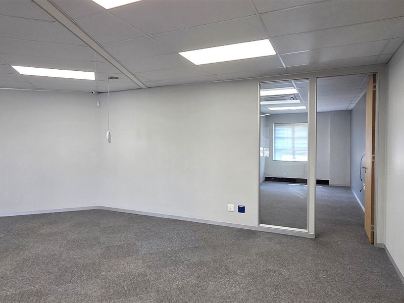 A bright, open-plan office space featuring neutral carpet tiles, a suspended ceiling with recessed lighting, and glass partitions for a modern, professional feel.