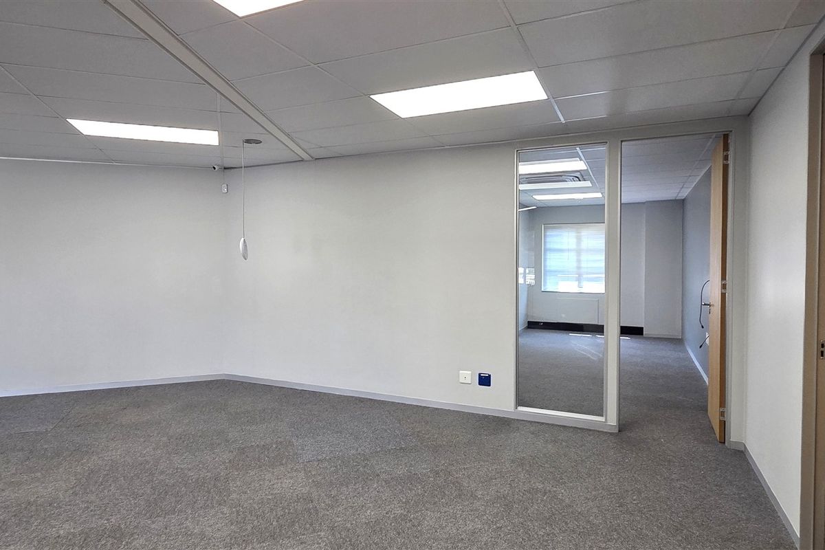 A bright, open-plan office space featuring neutral carpet tiles, a suspended ceiling with recessed lighting, and glass partitions for a modern, professional feel.