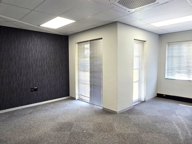A bright, empty office space featuring a modern accent wall, carpeted flooring, suspended ceiling with recessed lighting, and integrated air conditioning.