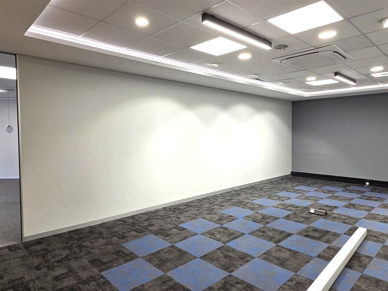 A modern, vacant office space featuring a suspended ceiling with recessed lighting, ducted air conditioning, and patterned carpet tiles.