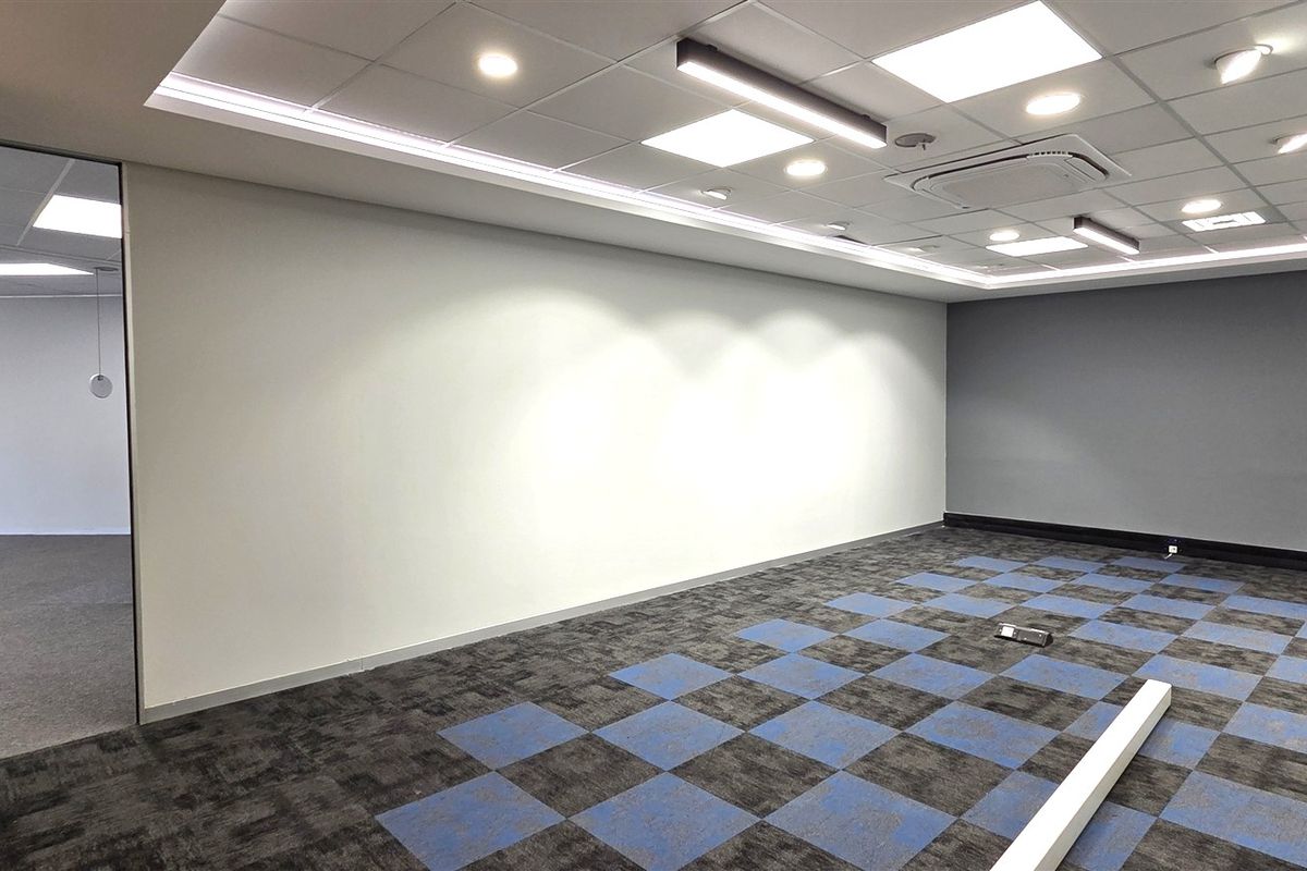 A modern, vacant office space featuring a suspended ceiling with recessed lighting, ducted air conditioning, and patterned carpet tiles.