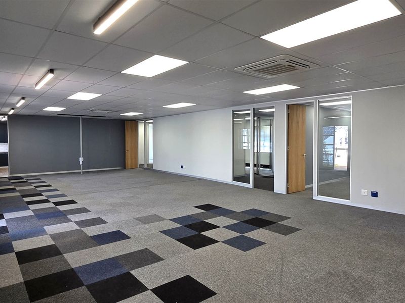 Spacious open-plan office area featuring modern carpet tiles, suspended ceilings with recessed lighting, and glass-partitioned private offices.