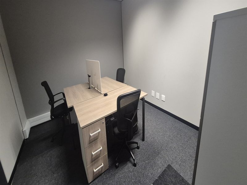 A compact, modern office space featuring neutral wall finishes, grey carpeting, and integrated electrical and data connectivity points.
