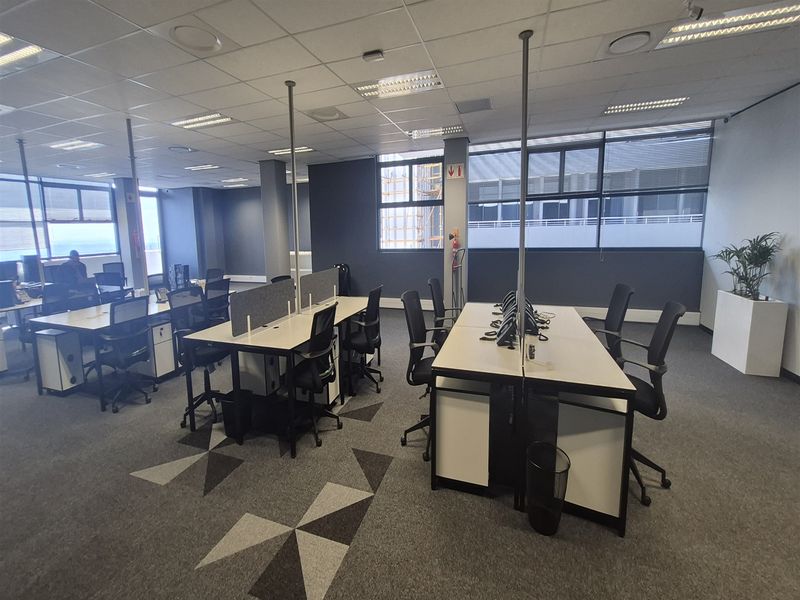 A professional open-plan office space featuring suspended ceilings, recessed lighting, large windows for natural light, and modern carpeted flooring.