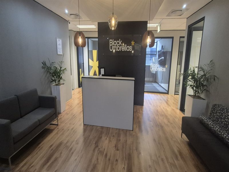 Modern office reception area featuring a central reception desk, wood-look laminate flooring, and glass-partitioned office spaces with contemporary pendant lighting.