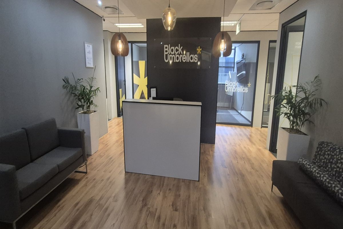 Modern office reception area featuring a central reception desk, wood-look laminate flooring, and glass-partitioned office spaces with contemporary pendant lighting.