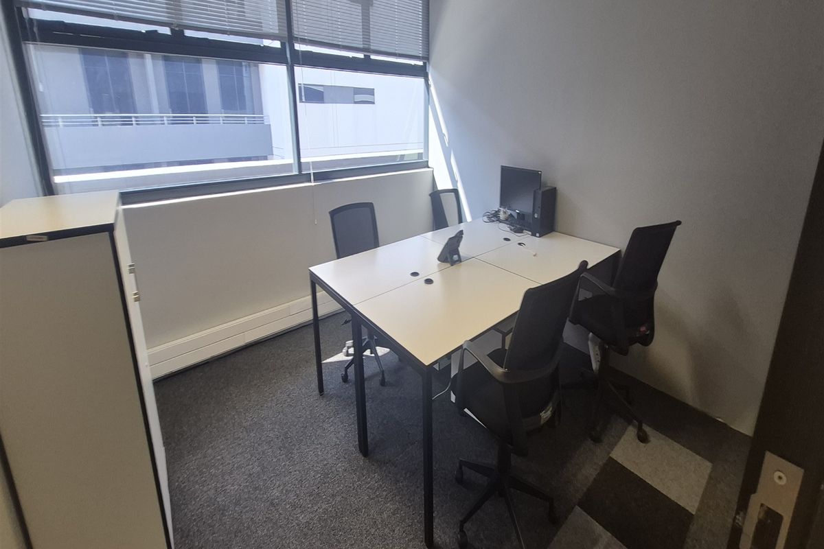 A functional office space featuring large windows with venetian blinds, carpeted flooring, and ample natural light, suitable for a professional work environment.