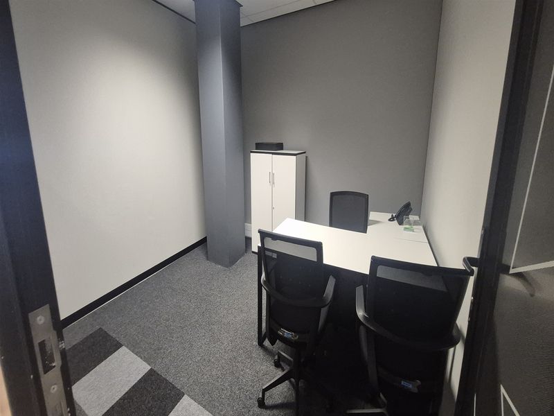 A compact, modern office space featuring neutral grey walls, carpeted flooring, and a prominent structural column.