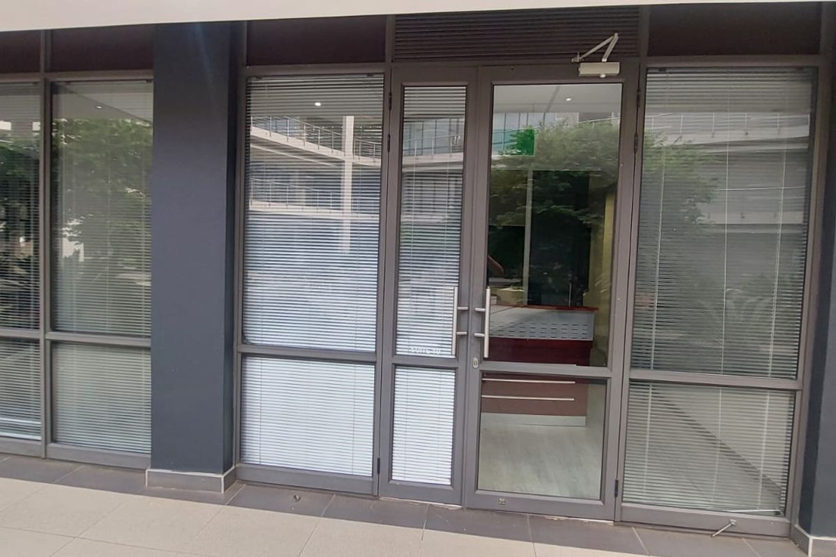 Commercial office entrance featuring modern aluminium-framed glass doors and partitioning with integrated blinds, providing a professional and transparent facade.