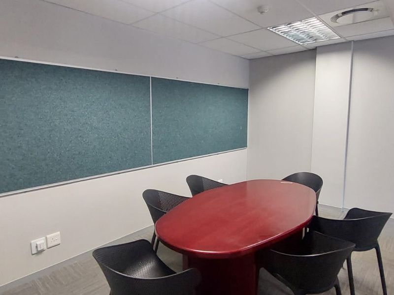 A functional office meeting room featuring a suspended ceiling, recessed lighting, wall-mounted pinboards, and carpeted flooring.