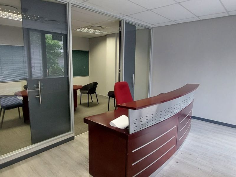 A professional commercial office space featuring a reception area, glass-partitioned private office, suspended ceilings, and modern laminate flooring.