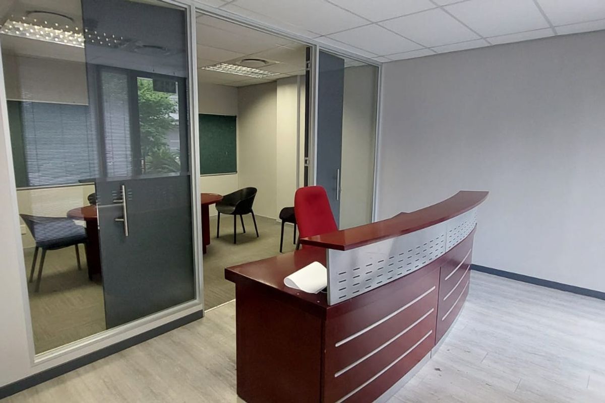 A professional commercial office space featuring a reception area, glass-partitioned private office, suspended ceilings, and modern laminate flooring.