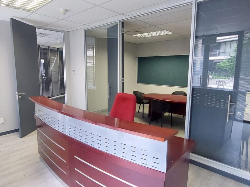 A professional commercial office space featuring a reception desk, glass-partitioned meeting room, suspended ceilings, and modern laminate flooring.