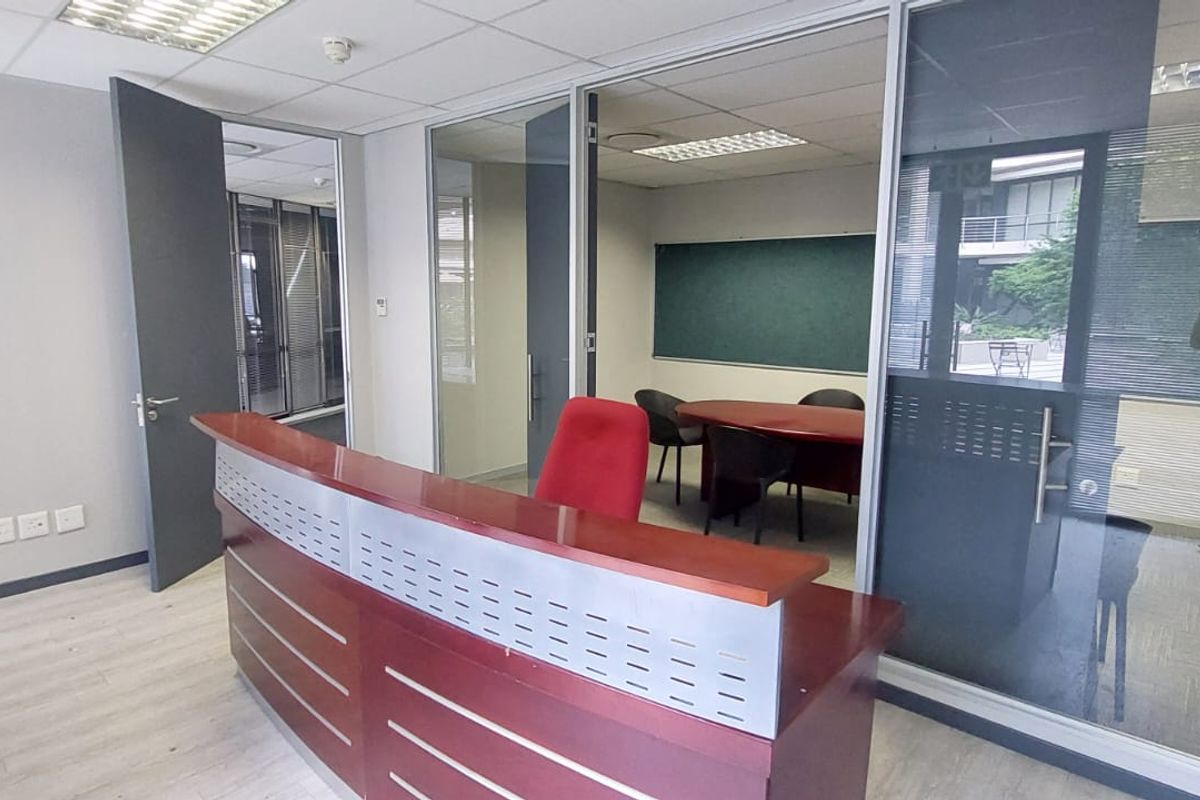 A professional commercial office space featuring a reception desk, glass-partitioned meeting room, suspended ceilings, and modern laminate flooring.