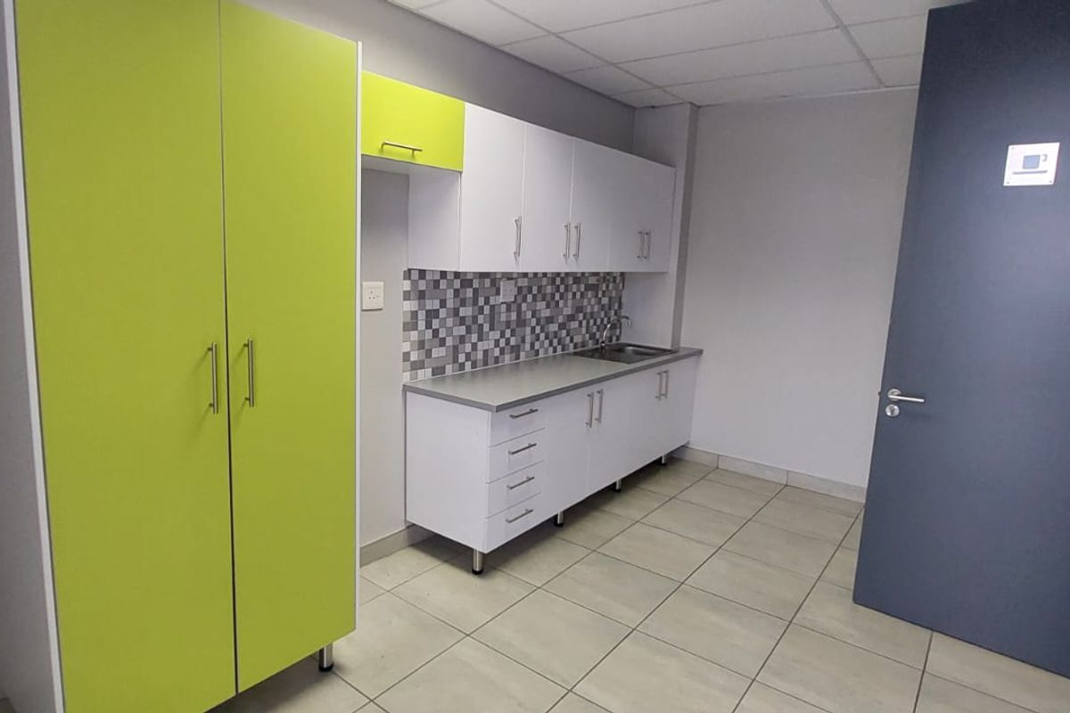 A clean, functional kitchenette featuring white and lime green cabinetry, a stainless steel sink, mosaic backsplash, and neutral tiled flooring.