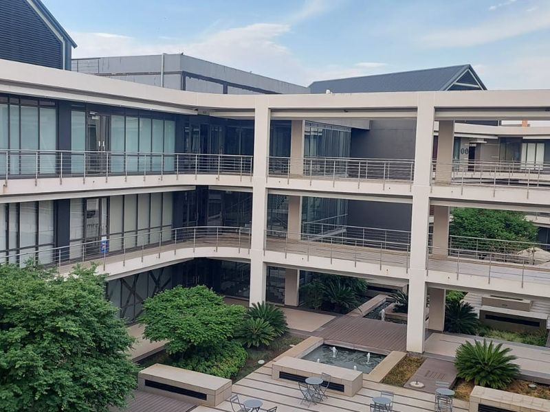 Modern multi-level commercial office complex featuring a central courtyard with a water feature, landscaped gardens, and extensive glass facade elements.