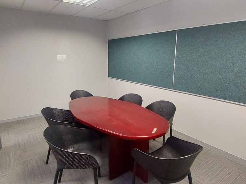 A functional office meeting room featuring carpeted flooring, a suspended ceiling with recessed lighting, and a large wall-mounted pinboard.