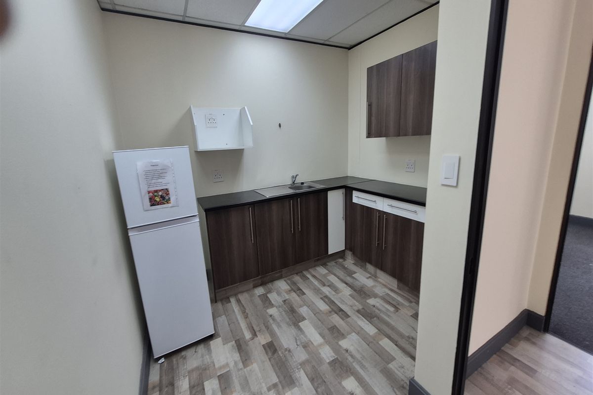 A compact office kitchenette featuring modern laminate cabinetry, a stainless steel sink, and durable wood-look laminate flooring under a drop ceiling.