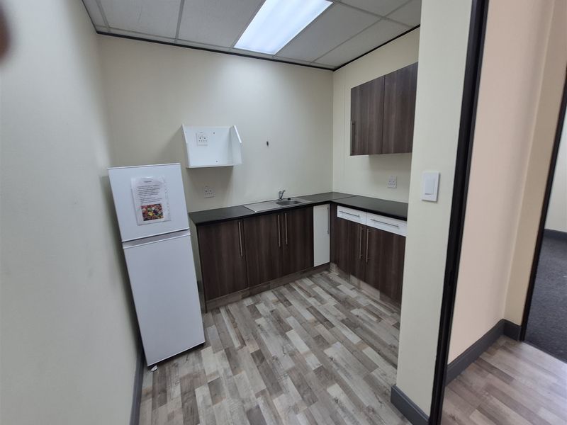 A compact office kitchenette featuring modern laminate cabinetry, a stainless steel sink, and durable wood-look laminate flooring under a drop ceiling.