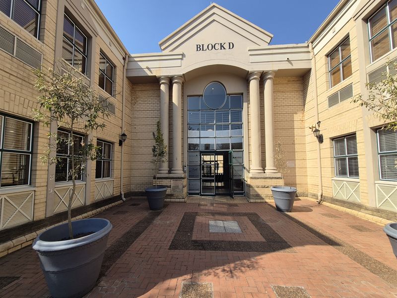 Front entrance view of Block D, featuring a paved courtyard, classical architectural columns, and a prominent glass-paneled office building facade.