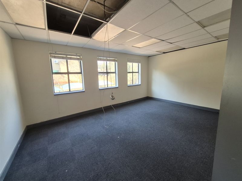 An empty office space featuring carpet flooring and a suspended ceiling with visible damage and missing tiles requiring repair.