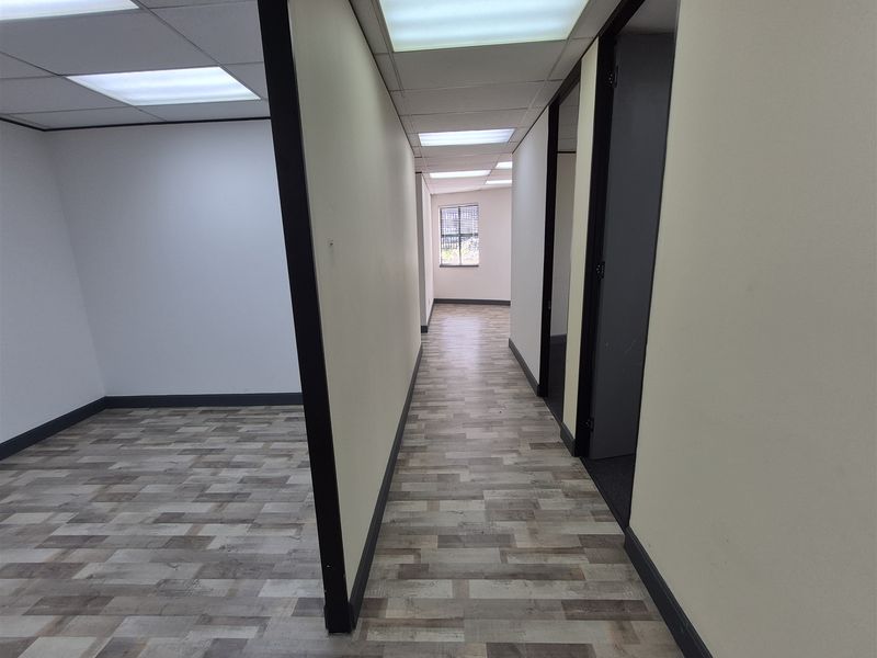 A clean, empty office hallway featuring modern laminate flooring, suspended ceilings with recessed lighting, and neutral wall finishes.