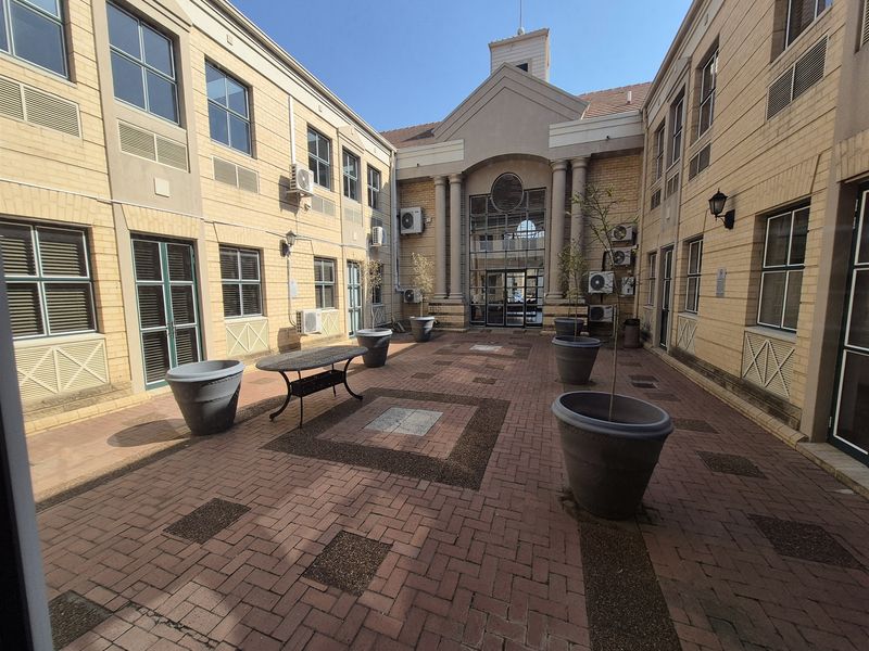 A well-maintained paved courtyard area between office building wings, featuring architectural columns, exterior air conditioning units, and integrated brickwork design.