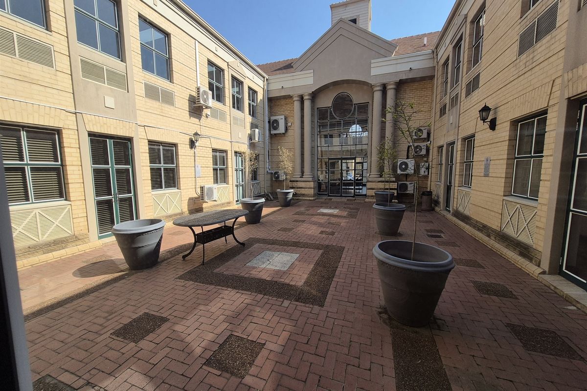 A well-maintained paved courtyard area between office building wings, featuring architectural columns, exterior air conditioning units, and integrated brickwork design.