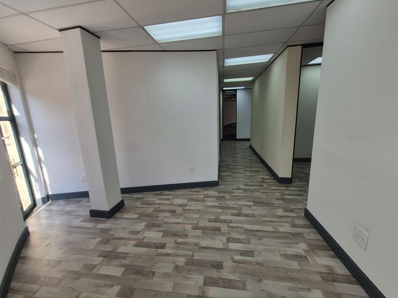 An empty, well-lit office space featuring modern laminate flooring, a suspended ceiling with recessed lighting, and a clean, neutral interior finish.